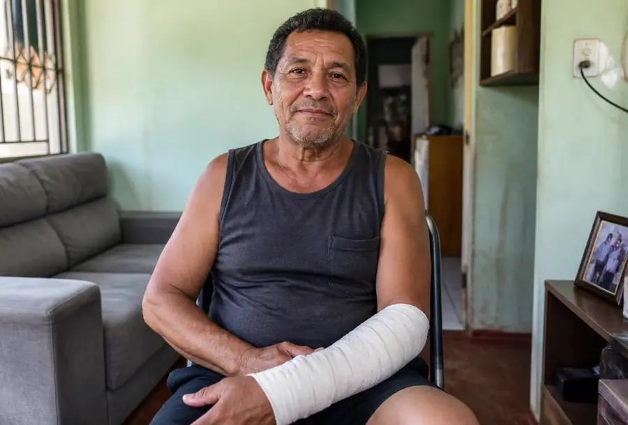 Homem adulto com o braço enfaixado sentado na sala de casa